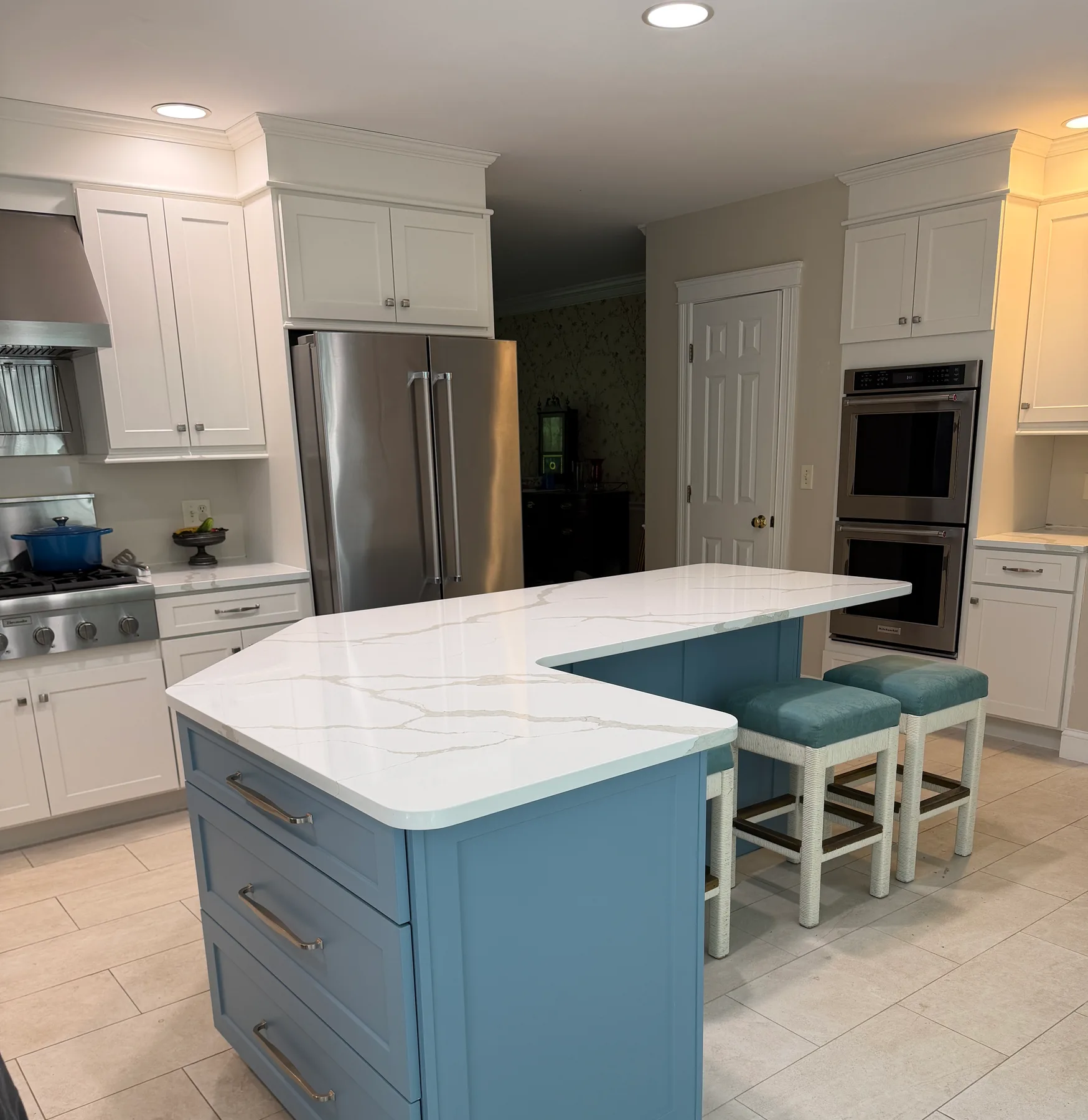 Blue-gray L-shaped kitchen island with white quartz waterfall countertop and woven counter stools