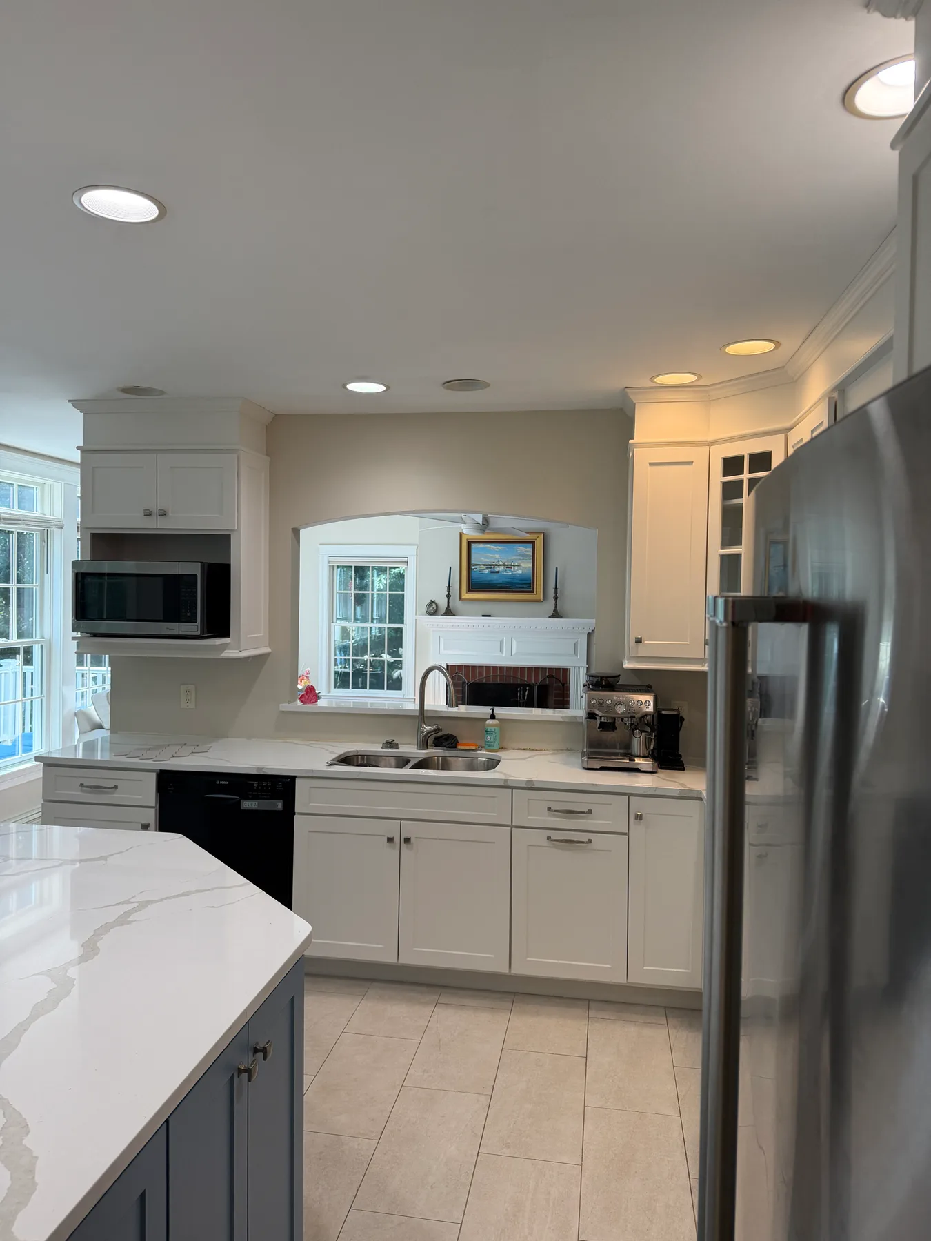 Kitchen sink wall with a pass-through opening to an adjoining room and the blue-gray island in the foreground