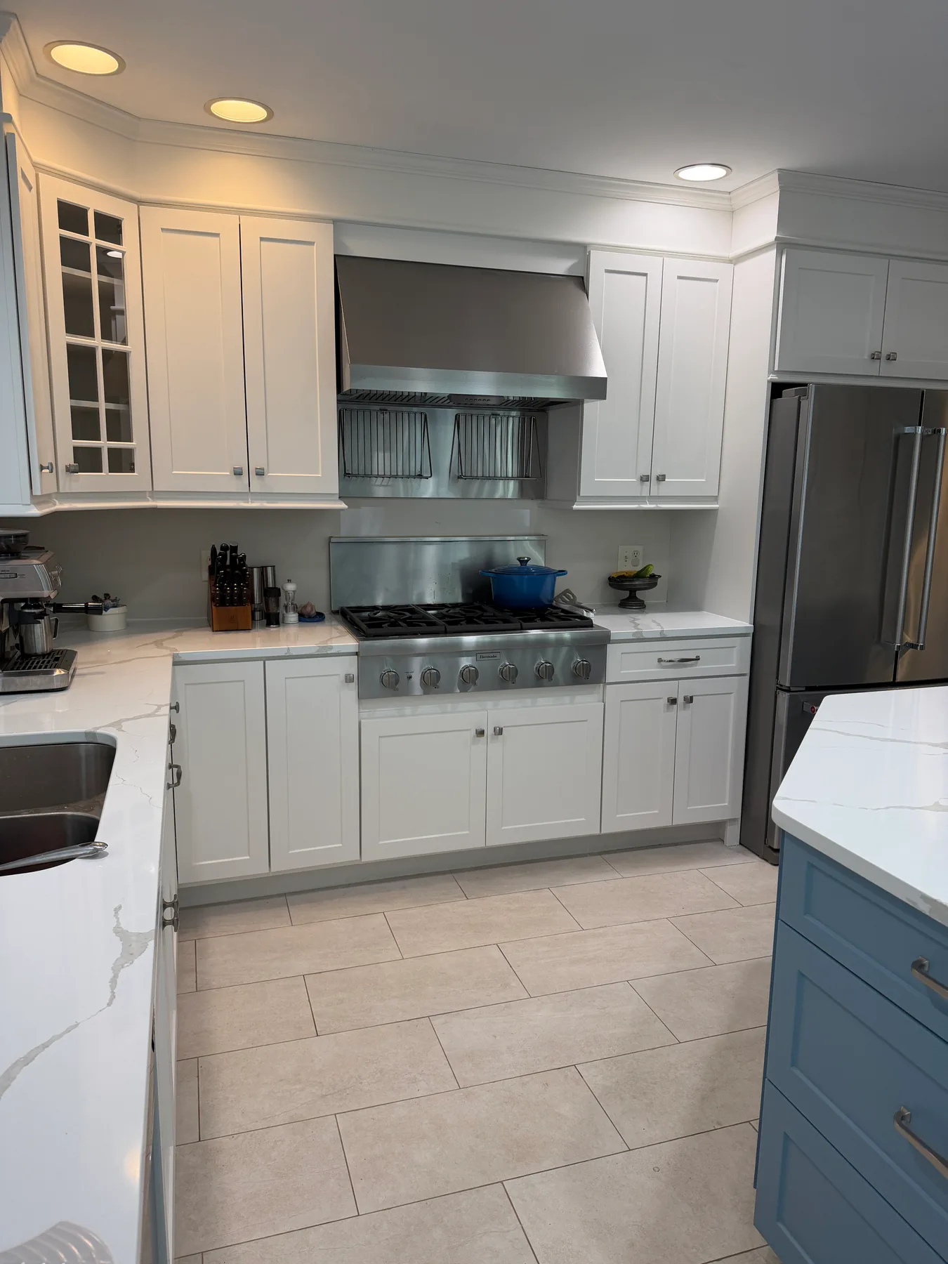 Straight-on view of the range wall with stainless hood, gas range, refrigerator, and the edge of the blue-gray island