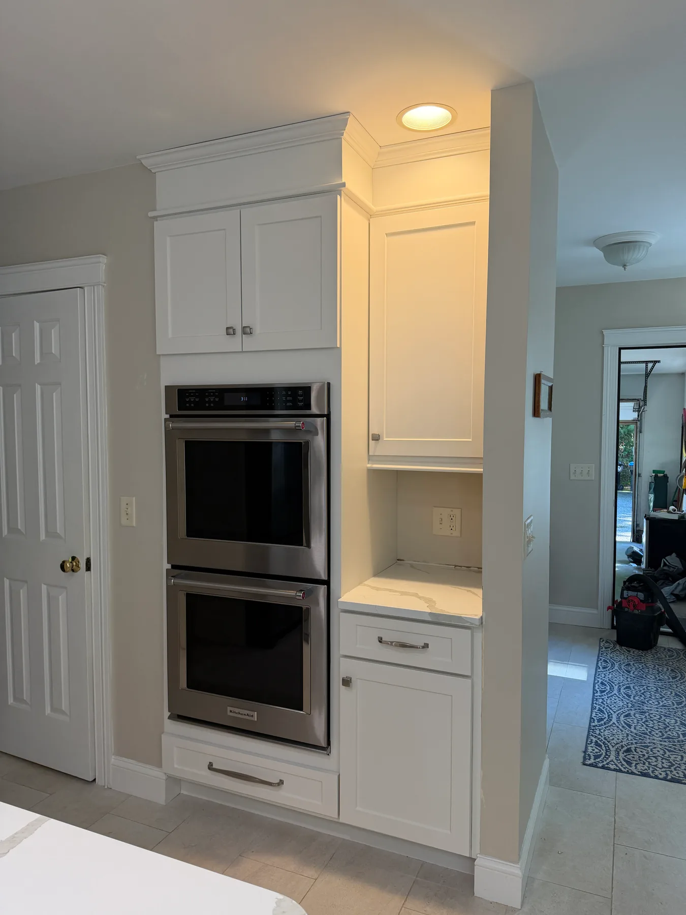 Stainless double wall ovens flanked by white cabinetry with an adjacent quartz counter niche