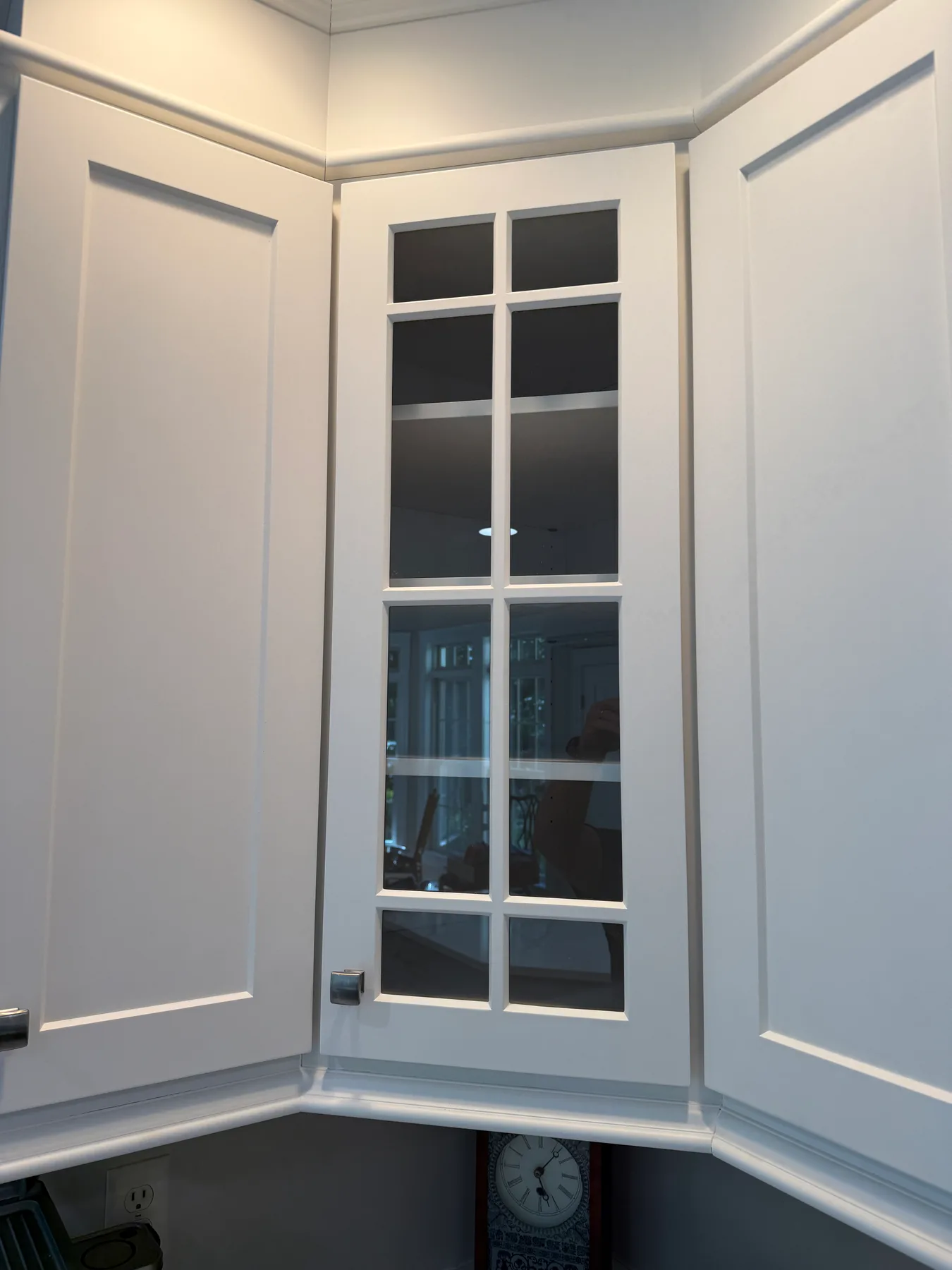 Detail of a tall glass-front corner cabinet with white shaker frame
